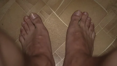 A top-down view of bare male feet on a tiled floor. 動画素材 342805635