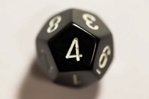 Top-down view of a black twelve sided die, showing a four 스톡 사진