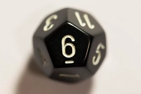 Top-down view of a black twelve sided die, showing a six Photos