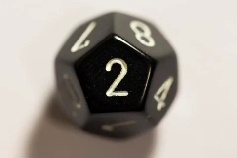 Top-down view of a black twelve sided die, showing a two Stock Photos