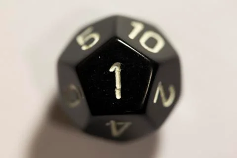 Top-down view of a black twelve sided die, showing a one Stock Photos