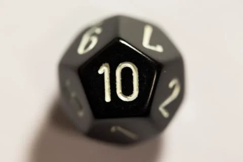 Top-down view of a black twelve sided die, showing a ten 스톡 사진