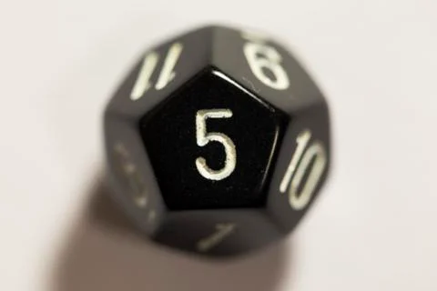 Top-down view of a black twelve sided die, showing a five Photos