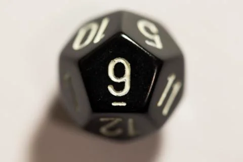 Top-down view of a black twelve sided die, showing a nine 스톡 사진