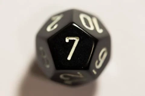 Top-down view of a black twelve sided die, showing a seven 스톡 사진