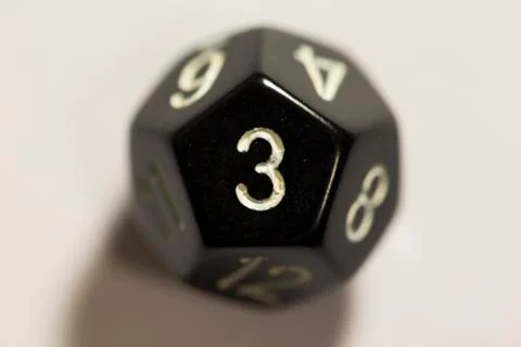 Top-down view of a black twelve sided die, showing a three 스톡 사진