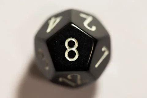 Top-down view of a black twelve sided die, showing an eight 스톡 사진