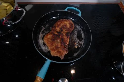Top-down view of a breaded meat cutlet frying in a pan on a modern black in.. Stock Photos