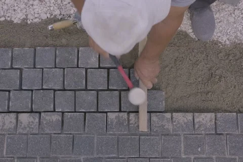 Top down view of a builder installing gray paving stones with a rubber mallet Stock Footage 345412407