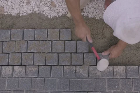Top down view of a builder laying gray paving stones on sand with a mallet Stock Footage 345412463