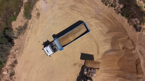 Top-down view of a bulldozer pushing sand into a semi-truck trailer at a sandy Stock Footage 336742819