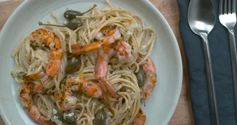 Top-down view of a chef's hand grates a lemon over a white plate of shrimp and o Stock Footage 199458039