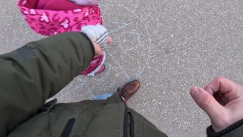Top-down view of child and adult playing hopscotch drawn with chalk on paved Stock Footage 313253504