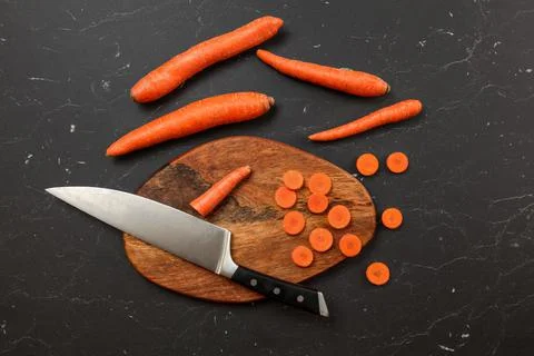 Top down view, chopping board, chef knife, and carrots, some of them cut in s Stock Photos