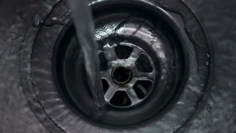Top down view of clear fresh water running down plug hole in metal sink Stock Footage 104784441