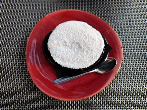 Top-down view of coconut ice cream in a dark bowl served on a red plate Stock Photos