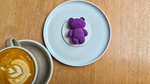 Top-down view of a cup of latte with latte art served beside a purple bear-shape Fotos de archivo