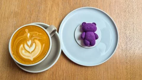 Top-down view of a cup of latte with latte art served beside a purple bear-shape Stock-Fotos