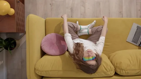 Top down view of cute generation z girl sits at home on yellow sofa in Stock Footage 248262707