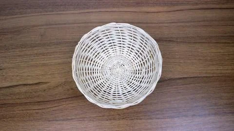 Top down view of an empty white wicker basket centered on a brown wooden ta.. 스톡 사진