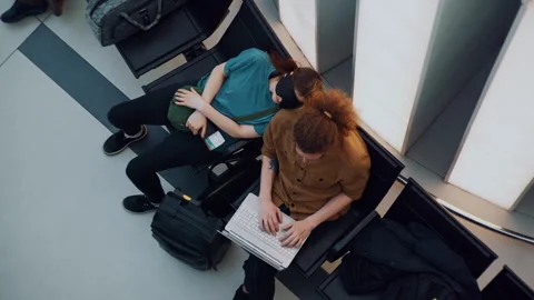 Top-Down View of Exhausted Young Travelers Napping on Bench in Airport Departure Video stock 334562609