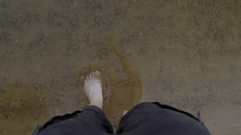 Top down view of feet entering river on shore of sandy beach. Ankles enter clear Stock Footage 221101082