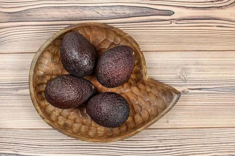 Top down view, four ripe avocados in wooden carved bowl, on wooden desk. Stock Photos