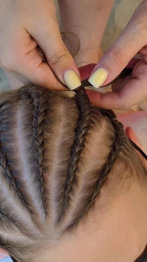 Top-down view of a hairstylist creating intricate cornrow braids. Stock Footage 314765011