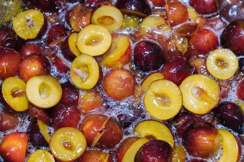 Top-down view of half of plums cooking in a bubbling syrup, making fruit jam or Stock Photos