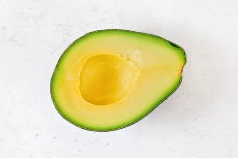 Top down view, halved avocado with yellow fruit pulp on white stone board Stock Photos