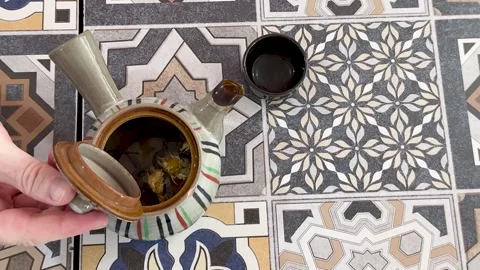 Top Down View of Hand Opening Ceramic Teapot on Patterned Table Stock Footage 329265086
