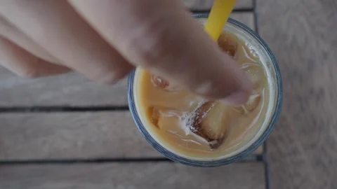 Top-down view of hand stirring iced coffee with a yellow straw on wooden tabl Stock Footage 331725635