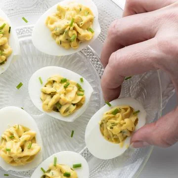 Top down view of a hand taking a deviled egg. Square crop. Stock Photos