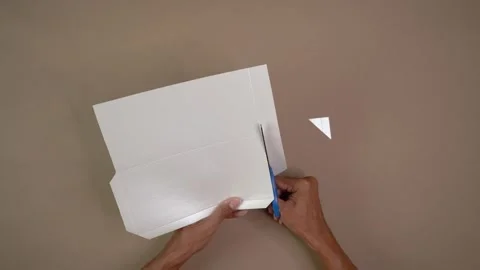 Top-down view of hands cutting folded white paper with scissors on neutral Stock Footage 344458836