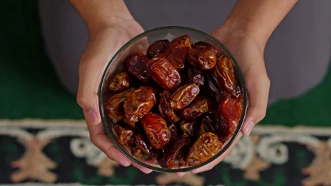 Top-down view of hands holding glass bowl of fresh organic dates over prayer mat Stock Footage 329103286