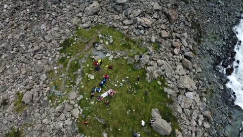 Top down view of hikers resting on green meadow near rocky mountain trail Stock Footage 335093629