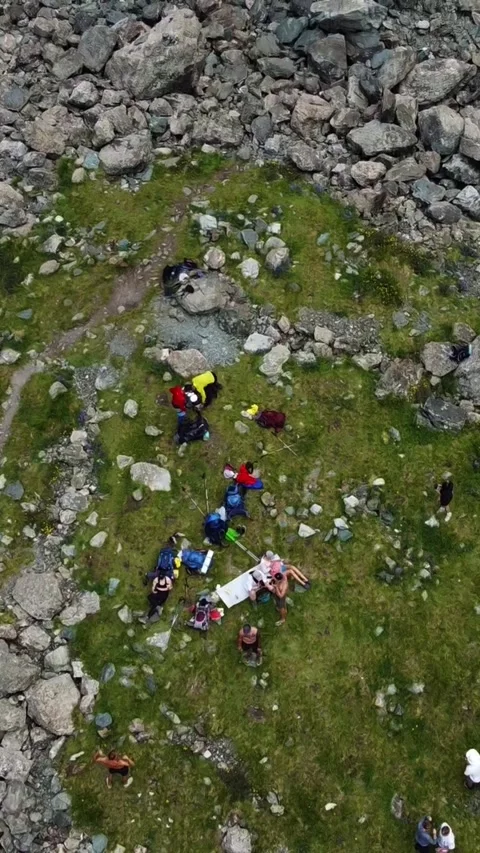 Top down view of hikers resting on green meadow near rocky mountain trail Video stock 336684832