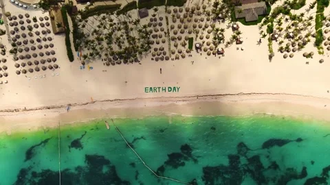 Top down view of large green title on tropical beach says EARTH DAY. People, sea Stock Footage 273870033