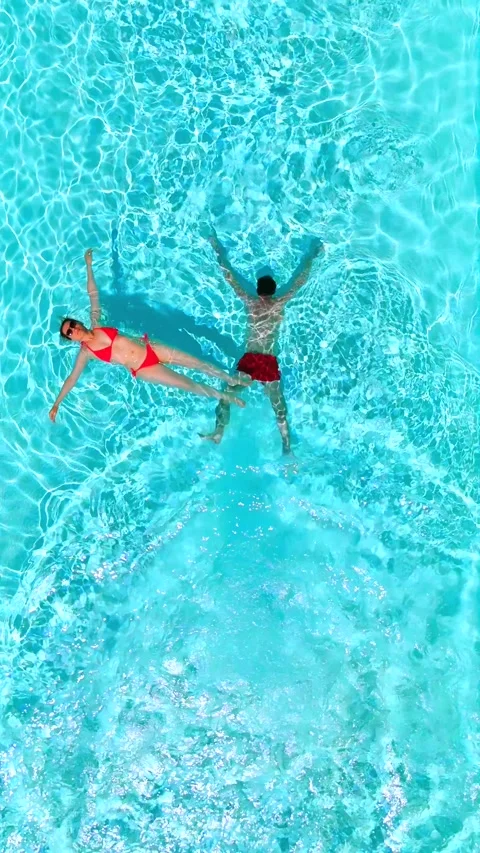 Top down view as a man dives into the pool while woman is laying on her back Video stock 326533646
