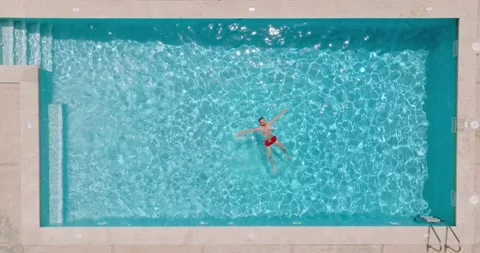 Top down view of a man in red shorts lying on his back in the pool. Stock Footage 210849171