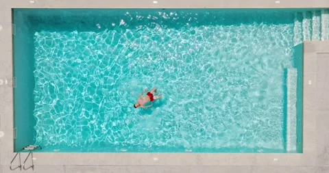 Top down view of a man in red shorts is lying on his back in the pool. Stock Footage 275084462