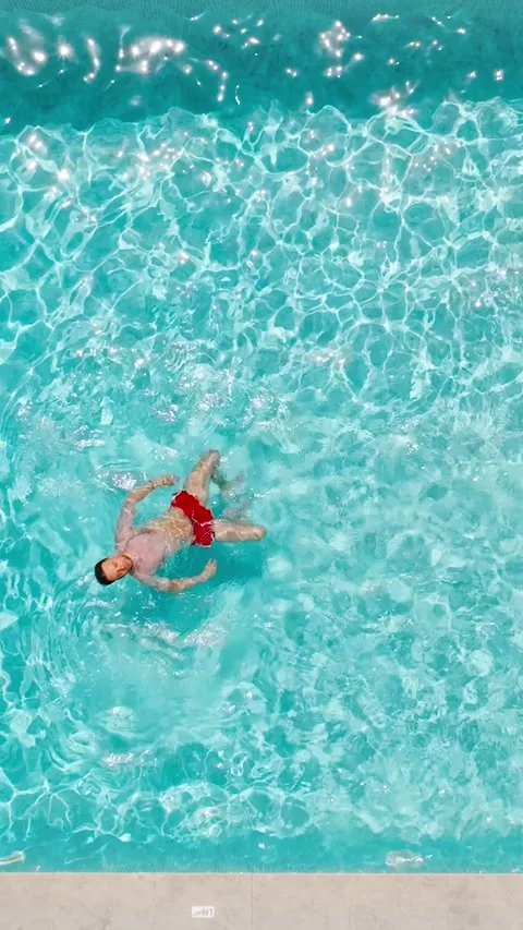 Top down view of a man in red shorts swims on his back in the pool. Stock Footage 317760954