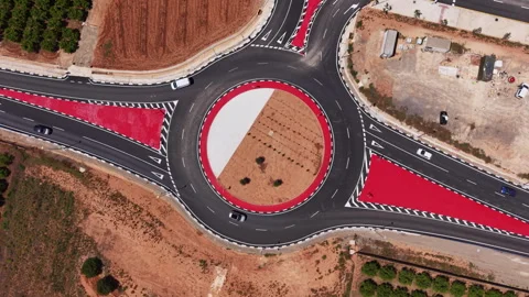 Top-down view of a modern roundabout with bold red painted zones, white dashed Stock Footage 343887003