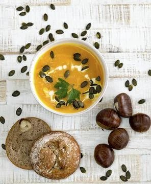 Top down view of organic pumpkin soup in a white bowl framed by chestnuts and Stock Photos
