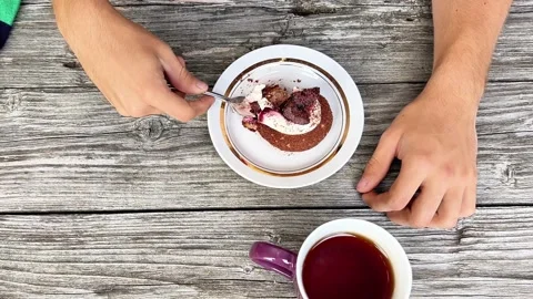 Top-Down View of Person Eating Chocolate Pastry with Fork and Tea on Wooden Stock Footage 345640228