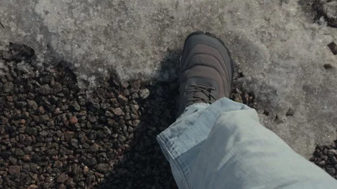 A top-down view of a person walking on gravel next to patches of melting snow. Stock Footage 330604757