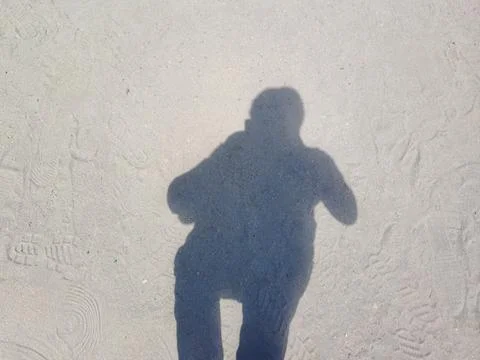 Top-down view of a person's full-body shadow on a sun-drenched sand beach. Stock Photos