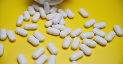 Top-Down View of Pills Spilling from White Bottle on Yellow Stock Footage 307862728