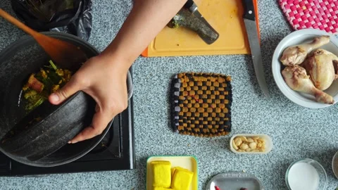 Top-down view of pouring freshly ground spice paste from mortar into heated pot Stock Footage 344910705