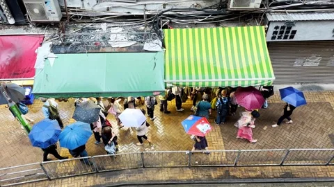 Top-Down View of Rainy Day Food Queue in Hong Kong with Passing Umbrellas Stock Footage 245913124